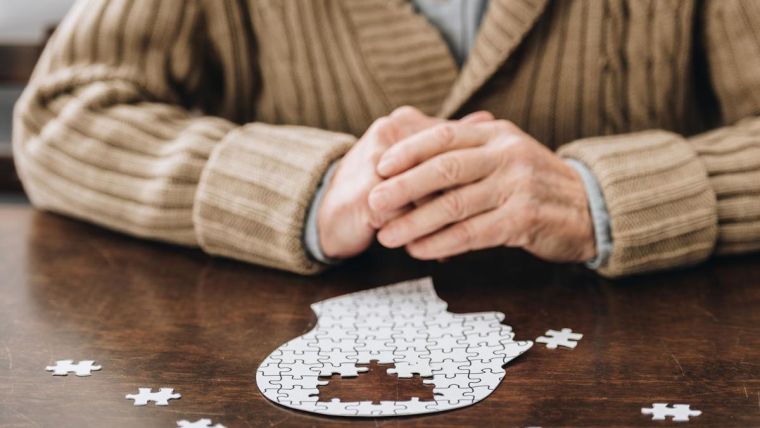 Image of an elderly person doing a jigsaw of a head shape, the 'brain' area of the jigsaw is missing.
