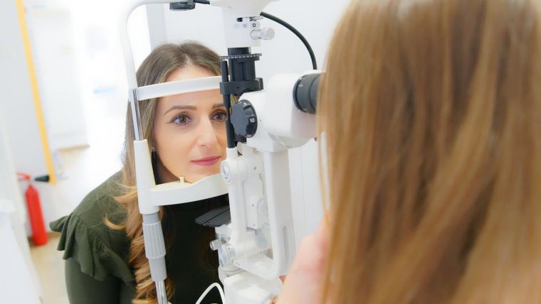 Optician looking into a ladies eyes using a ophthalmoscope to check eye health